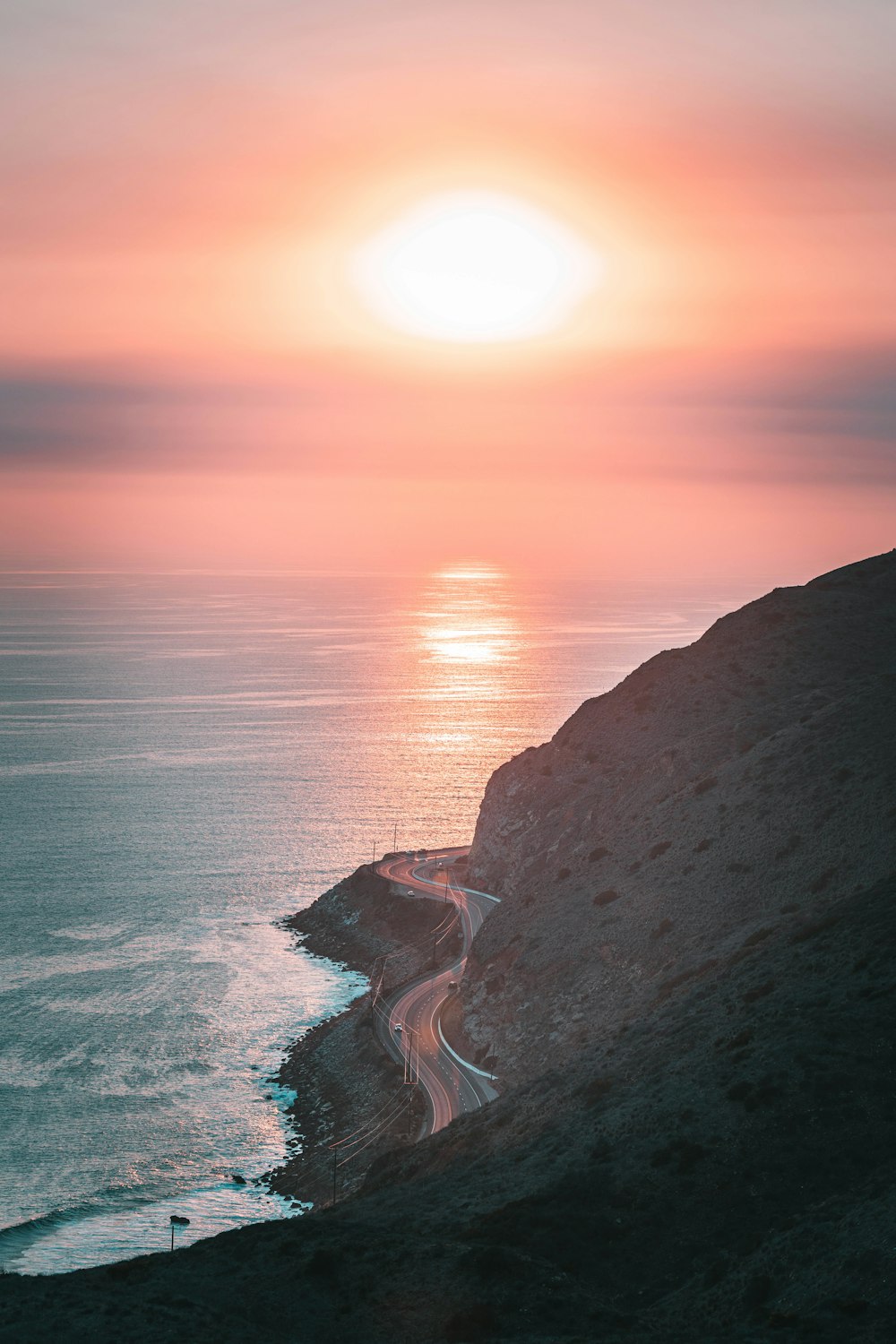 the sun is setting over the ocean and the road is empty