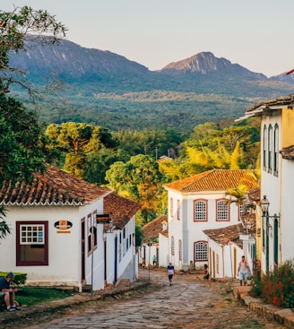 a cobblestone street with white buildings and mountains in the background