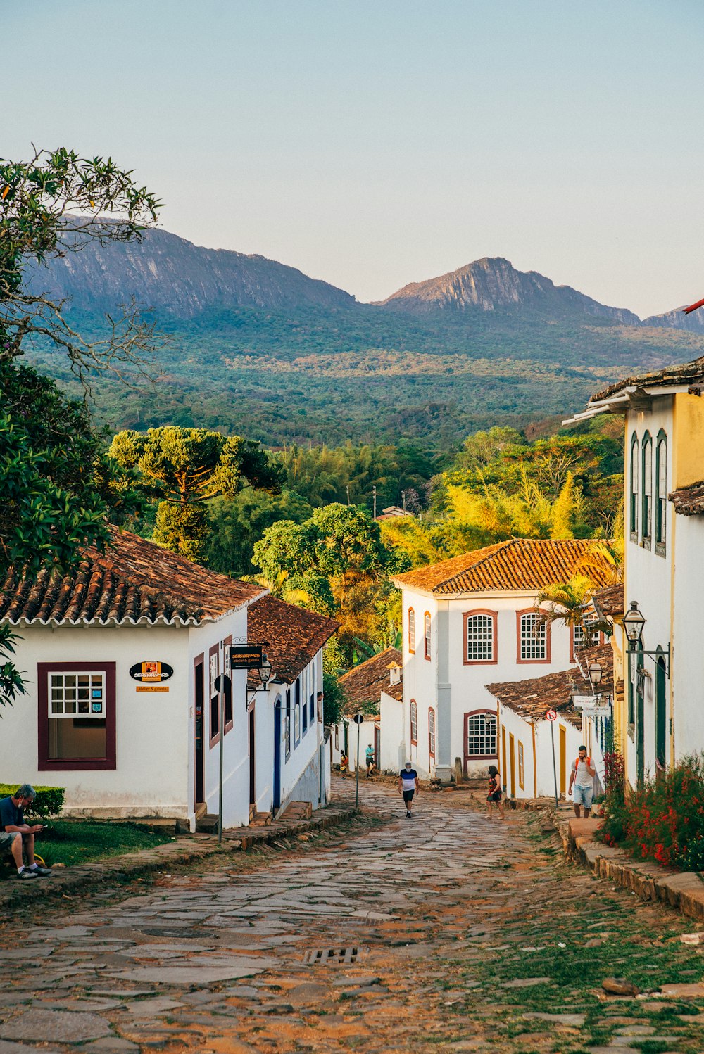 a cobblestone street with white buildings and mountains in the background