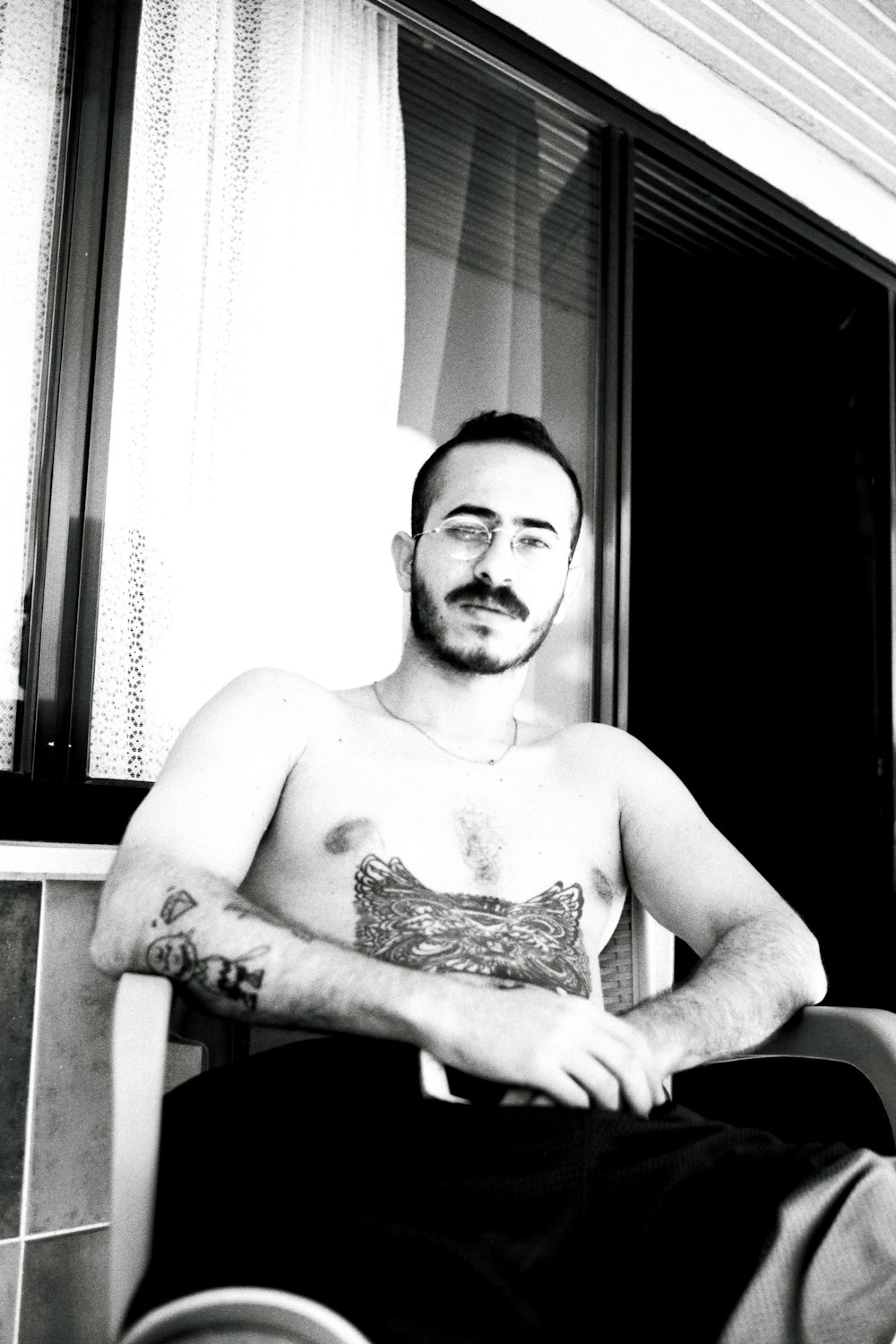 a shirtless man sitting in a chair in front of a window