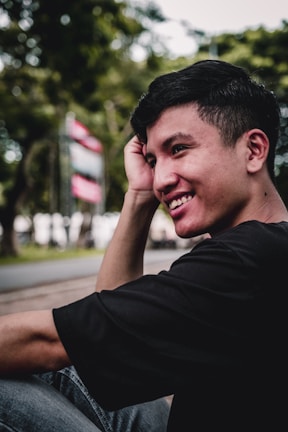 A charming young man smiling warmly in a city park.