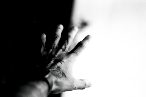 Dark, moody photo of a tattoo artist's hand holding a needle, with glowing red accents and deep shadows.
