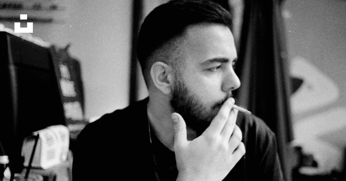 A man sitting in front of a computer desk smoking a cigarette photo ...
