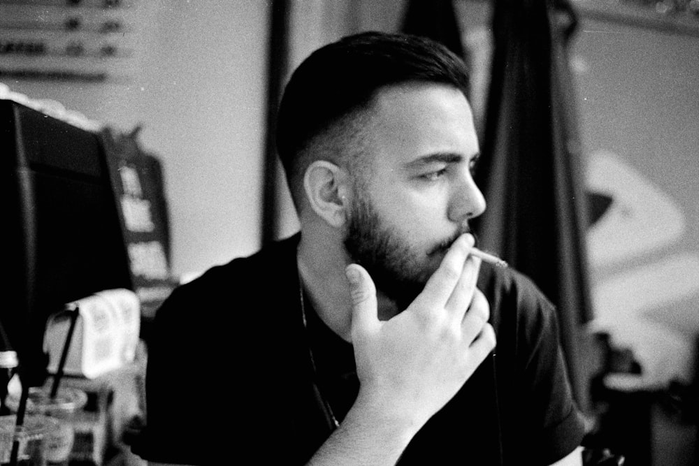 a man sitting in front of a computer desk smoking a cigarette