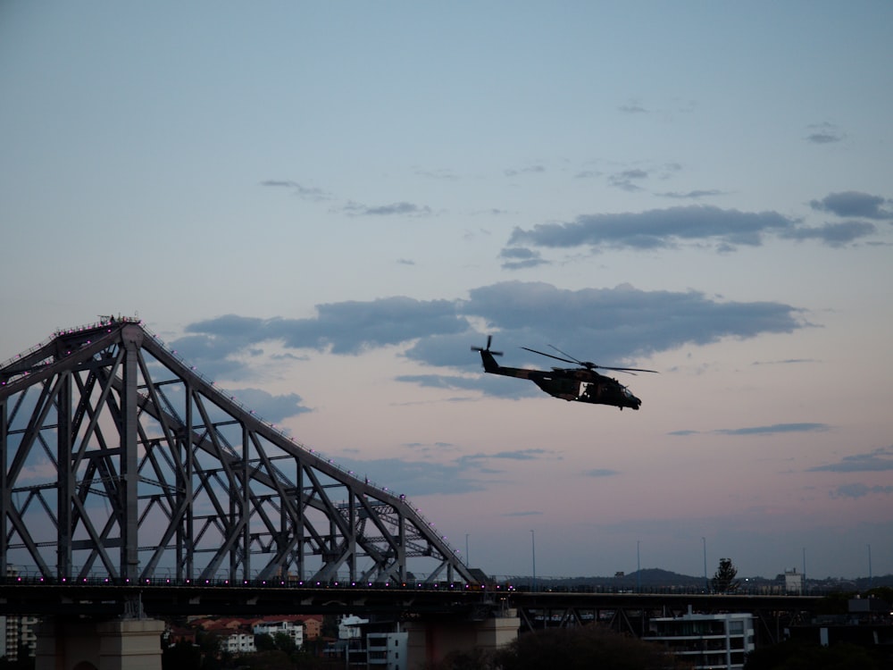 Ein Hubschrauber fliegt in der Abenddämmerung über eine Brücke