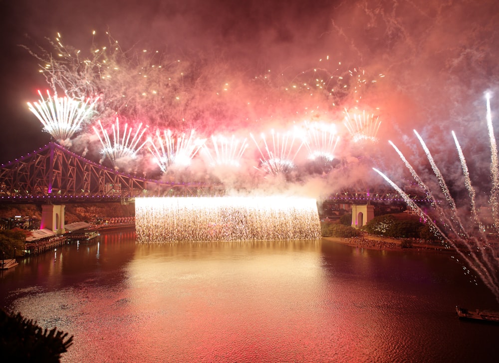 a large fireworks display over a river with a bridge in the background