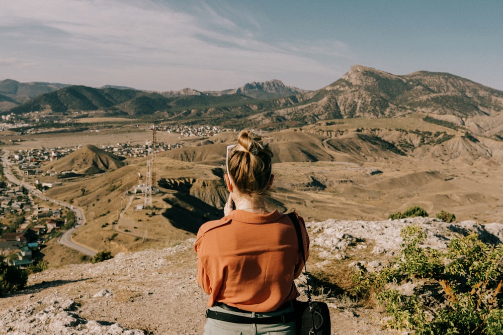 a woman sitting on top of a hill overlooking a valley