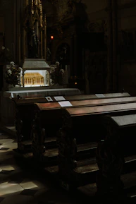 Interior of a church showing wooden pews and an ornate altar with candles lit.