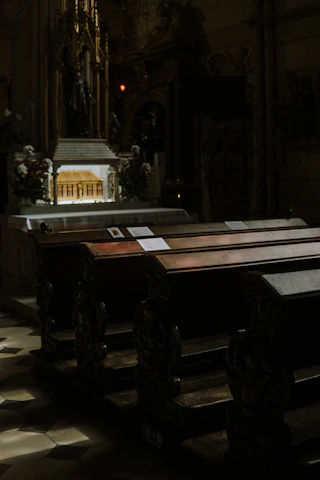 Interior of a church showing wooden pews and an ornate altar with candles lit.
