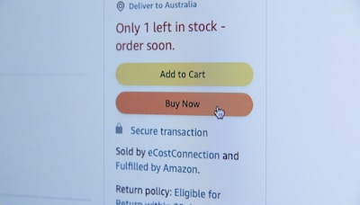 A screenshot of an online shopping webpage displaying a notification that only one item is left in stock and suggesting to order soon. There are two buttons, 'Add to Cart' in yellow and 'Buy Now' in orange, with a cursor hovering over the 'Buy Now' button. Additional text includes information about secure transactions and delivery options.