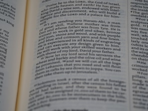A close-up view of an open book page displaying text in English. The layout appears to be similar to that of a religious or classical text, possibly a Bible, as indicated by the column format and verse numbers. The text discusses a message regarding a skilled individual named Huram-Abi and refers to craftsmanship in various materials.