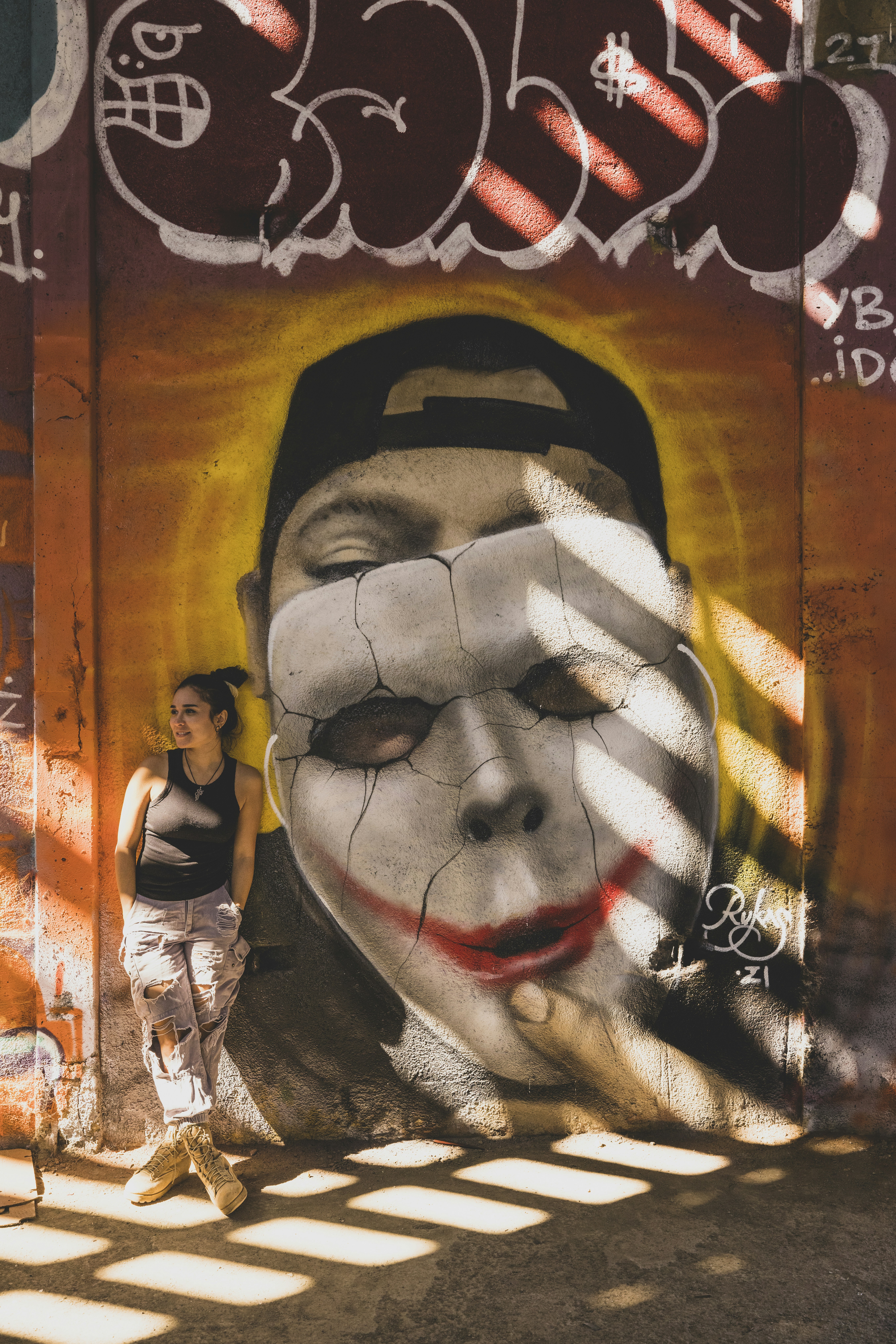 Mujer apoyada en una pared exterior con un mural de grafiti.