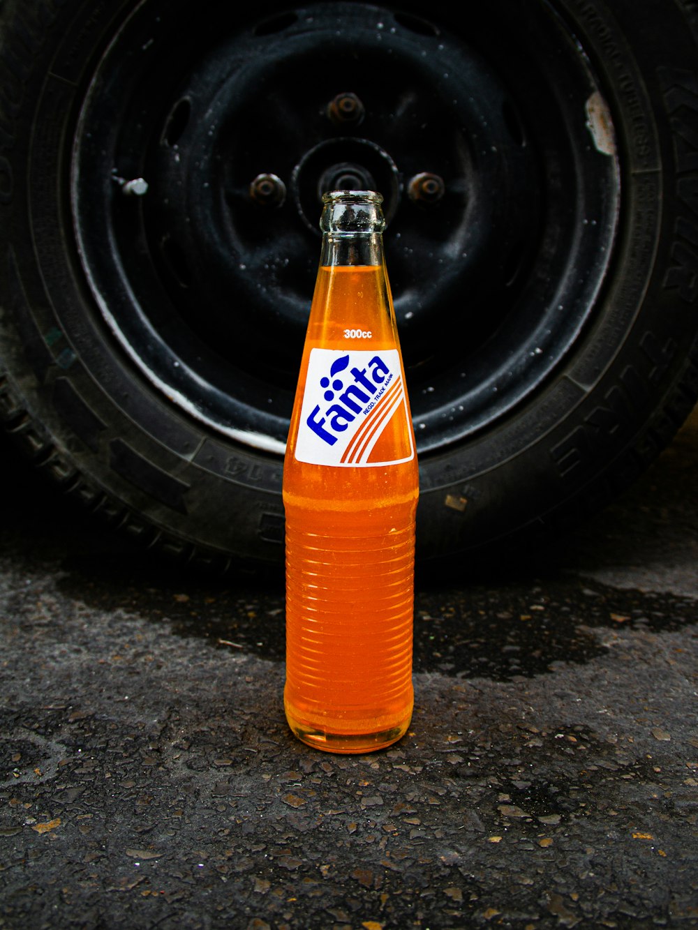 una bottiglia di soda seduta a terra accanto a un pneumatico