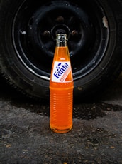 a bottle of soda sitting on the ground next to a tire