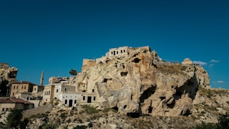 Ancient cave city ruins nestled in the rugged Caucasus foothills under a clear blue sky.