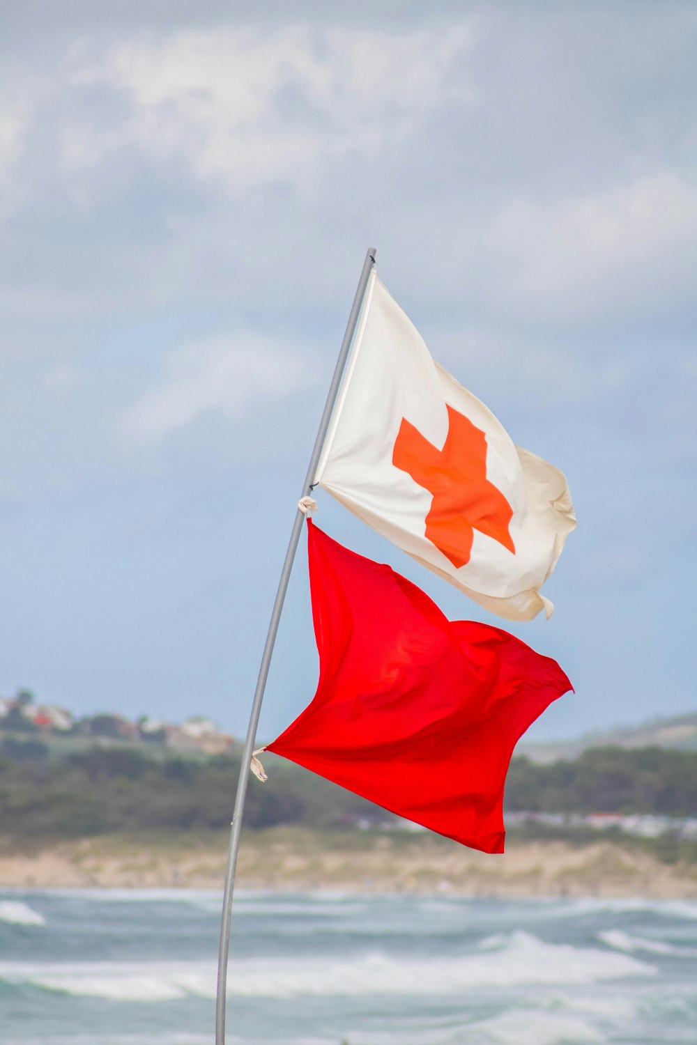 a red and white flag on a beach next to the ocean