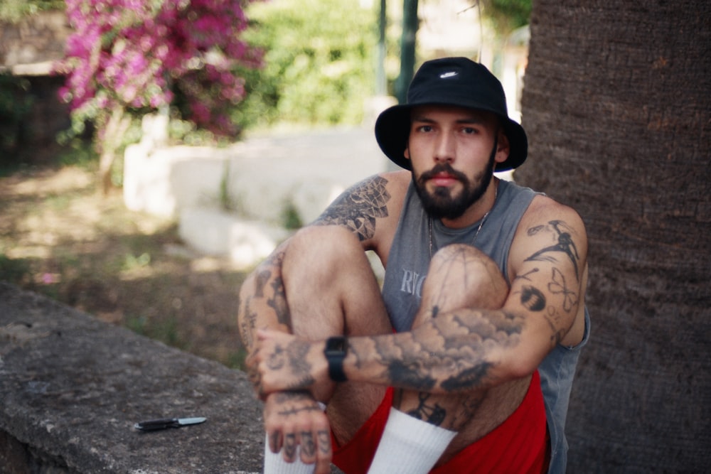 a man with tattoos and a hat sitting on a ledge