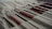 A set of paintbrushes neatly arranged in a fabric holder, showcasing a variety of sizes and colors. The brushes have red and black handles with metallic ferrules, lying against a soft, cream-colored fabric which provides a gentle backdrop.
