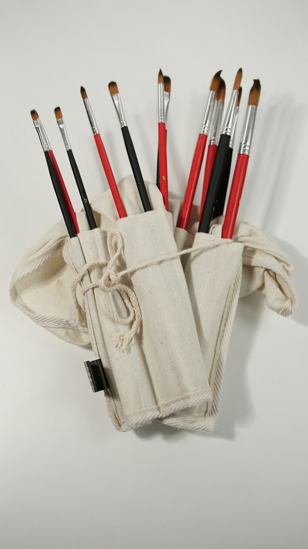 a white pouch with a dozen red and black brushes in it