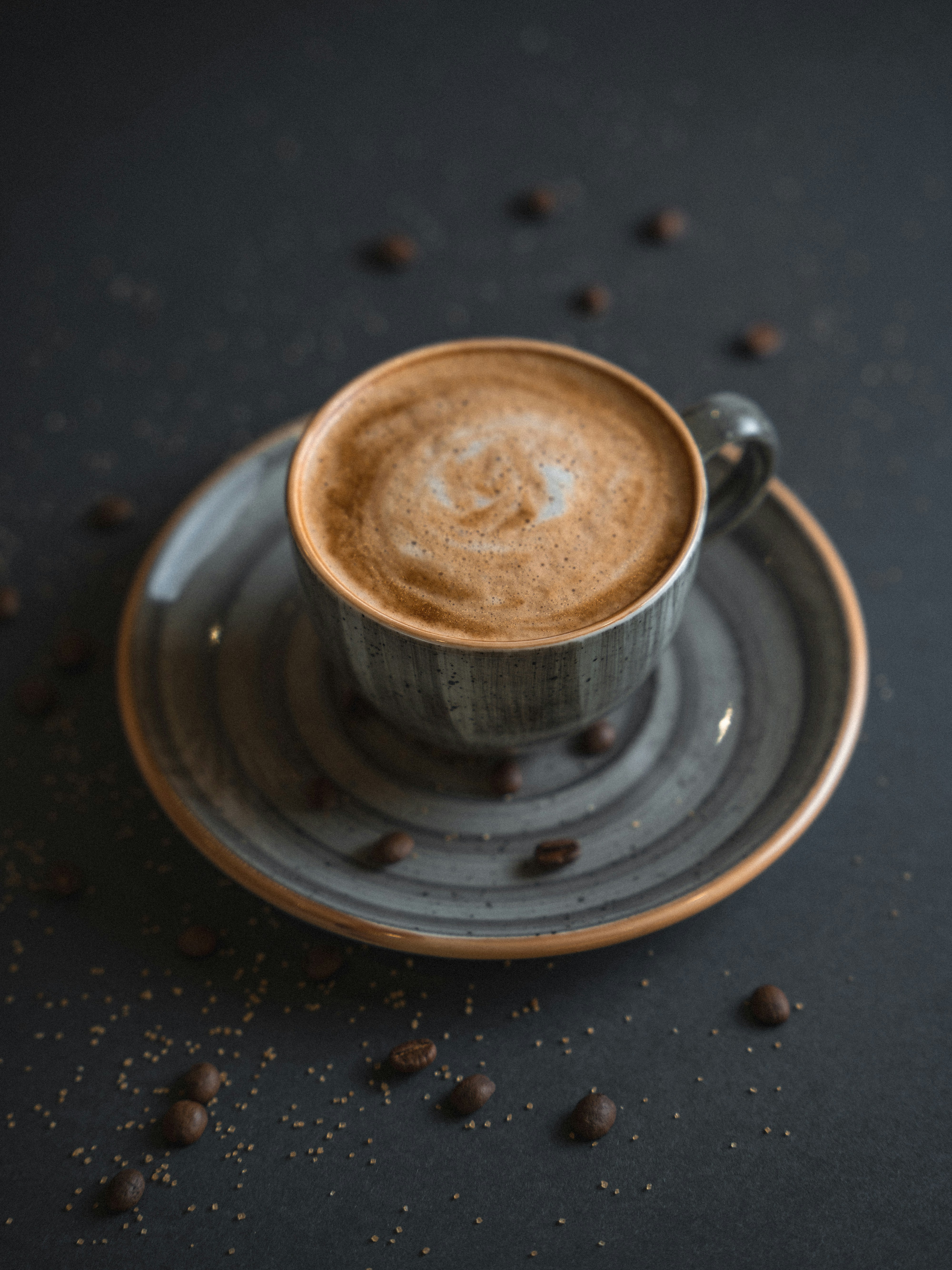 a cup of coffee on a saucer with coffee beans scattered around it