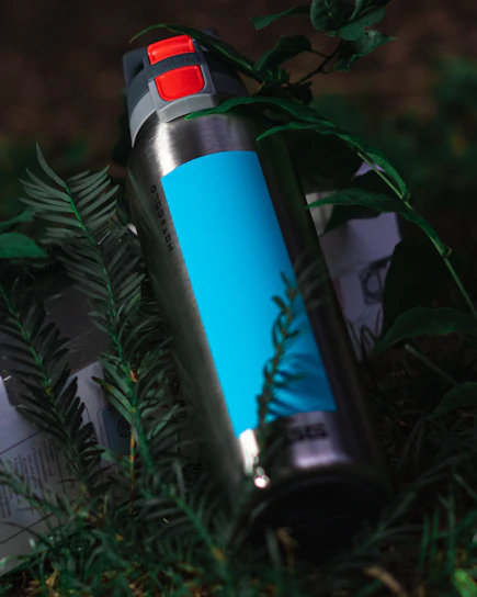 A sleek navy-blue insulated water bottle resting on a wooden picnic table with sunlight filtering through trees.