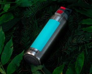 A vibrant turquoise water bottle with a flip-top lid, surrounded by fresh green leaves.