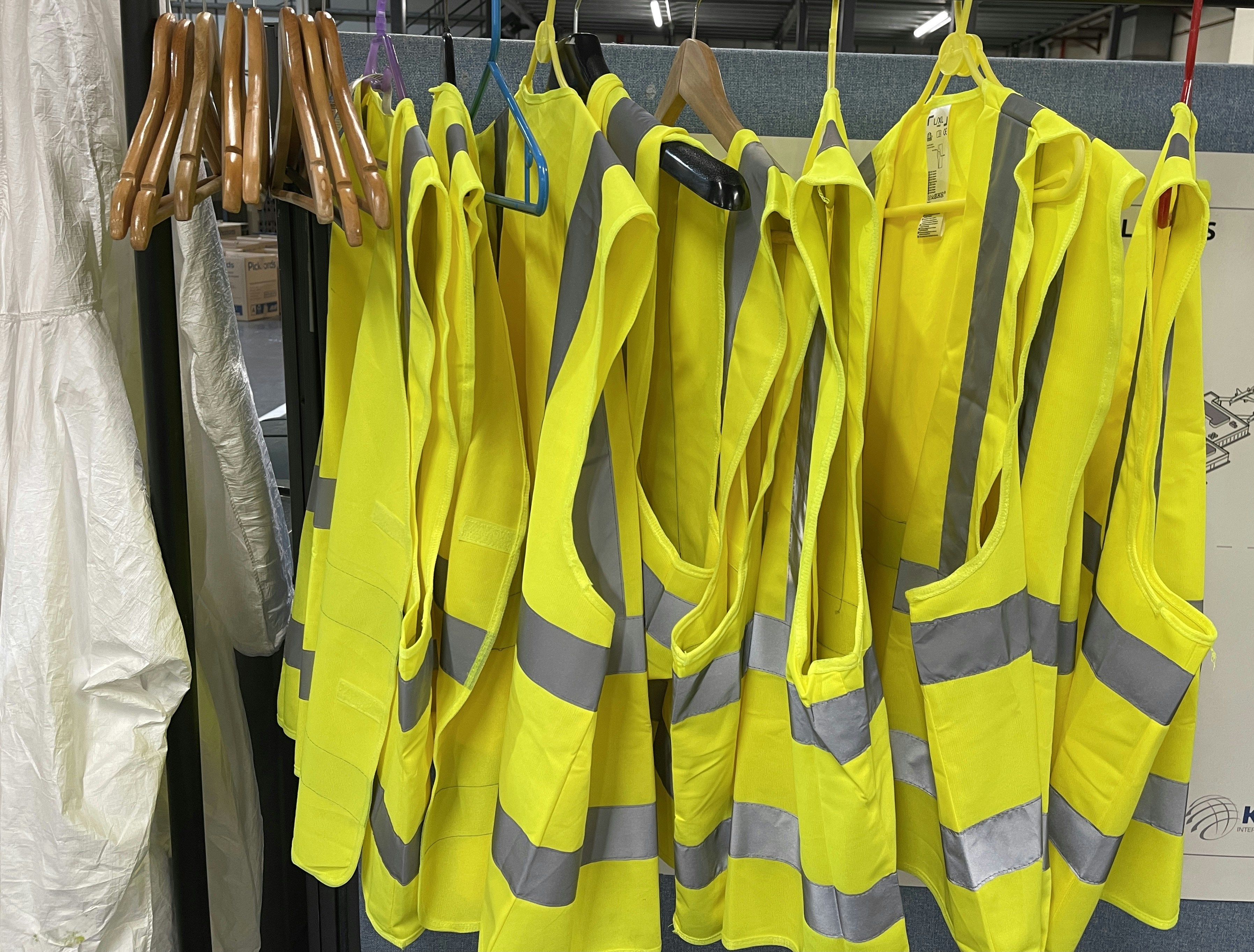Bright orange and yellow reflective safety vests hanging on rack in industrial warehouse, strong overhead lighting