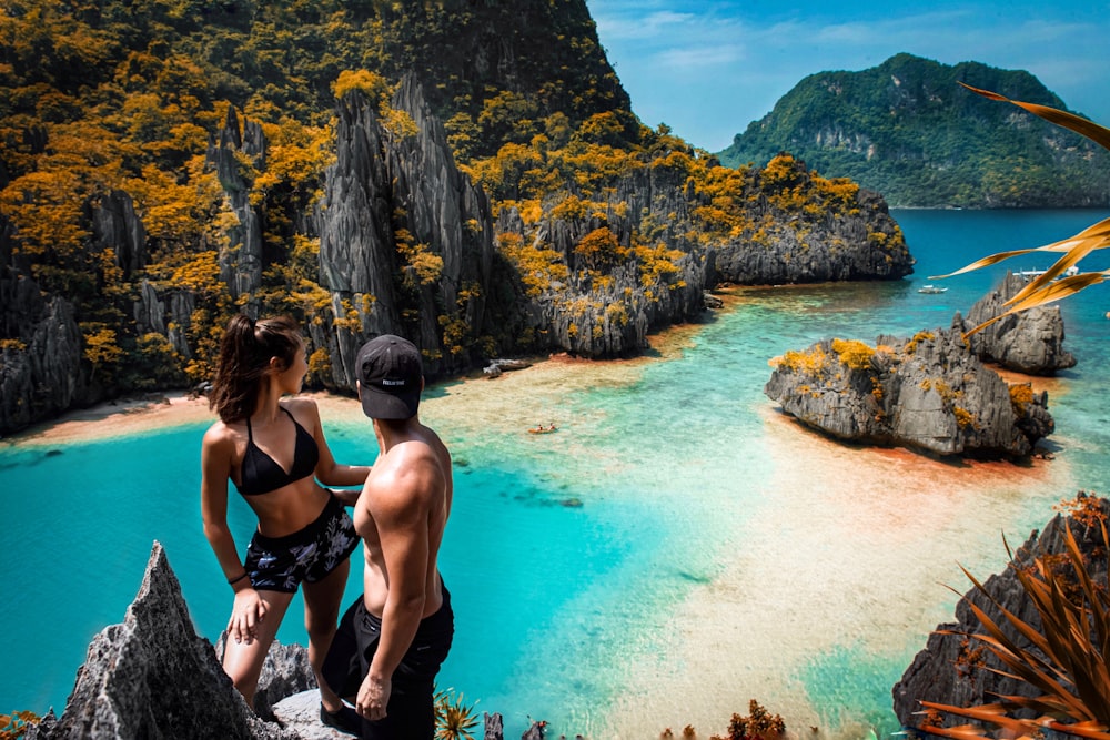 a man and a woman sitting on a rock looking at the ocean