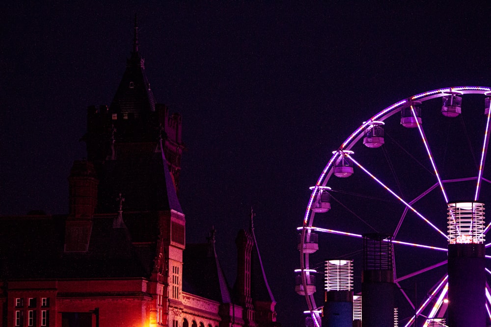 a ferris wheel lit up at night with buildings in the background