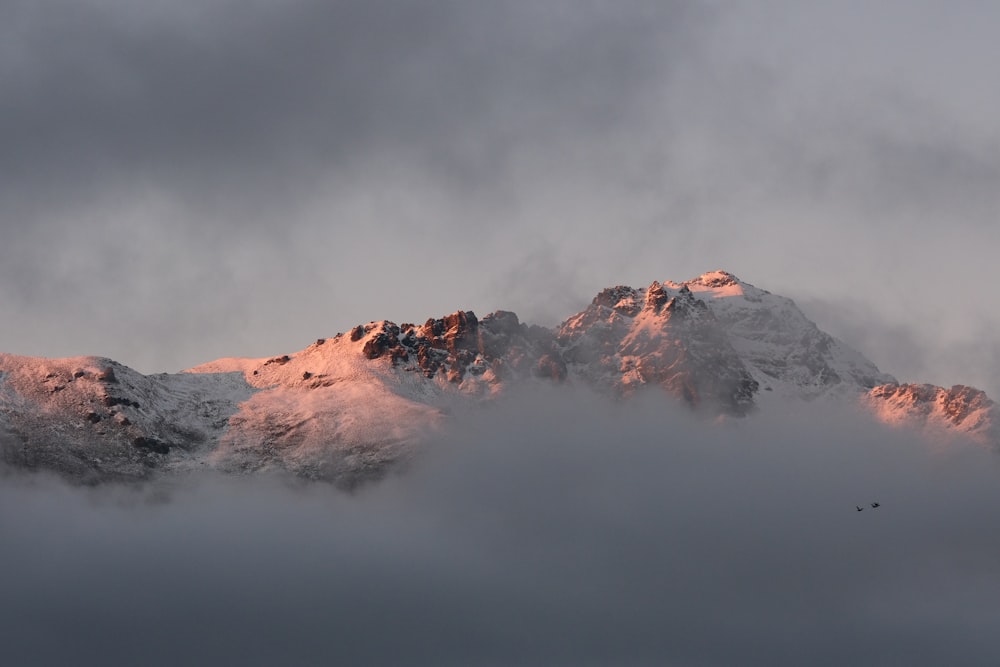 a mountain covered in snow and clouds under a cloudy sky