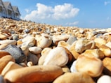 Wide view of a beach pebble quarry with workers selecting stones under a clear sky.