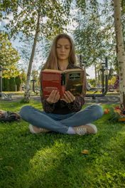 a woman sitting in the grass reading a book