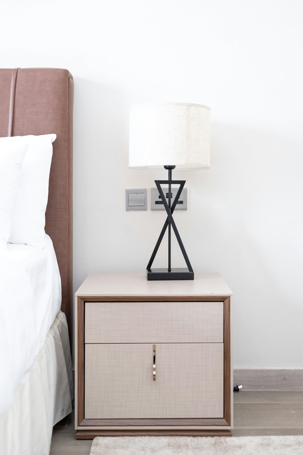 a nightstand with a lamp on top of it next to a bed