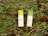 Two rectangular packages of Lamacoppa Leaf Sciences full spectrum hemp extract lie on a bed of green foliage and red clover flowers. The packaging is primarily green and white with floral designs and text indicating the product details.