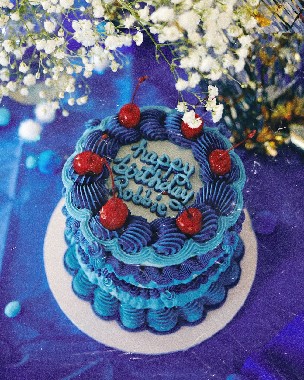 a blue birthday cake with cherries on top