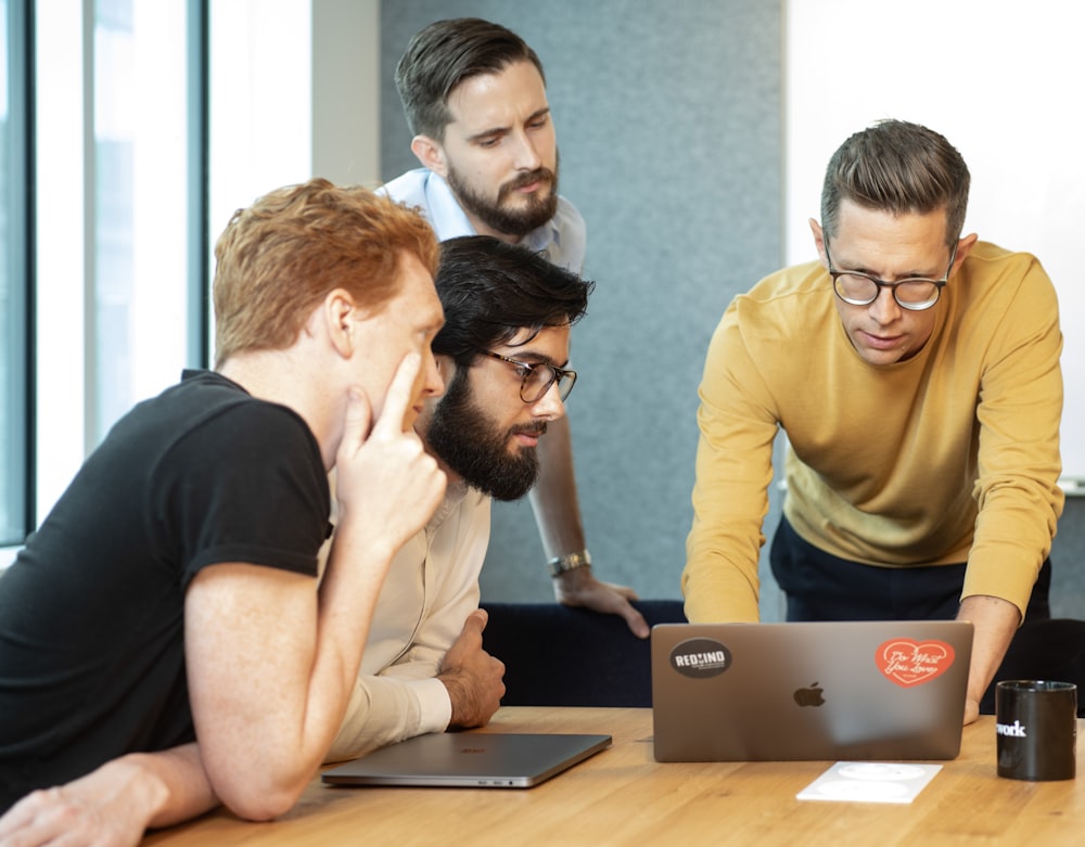 a group of men sitting around a table looking at a laptop