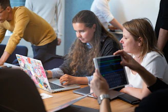 a group of people sitting around a table with laptops