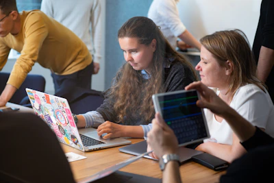 a group of people sitting around a table with laptops