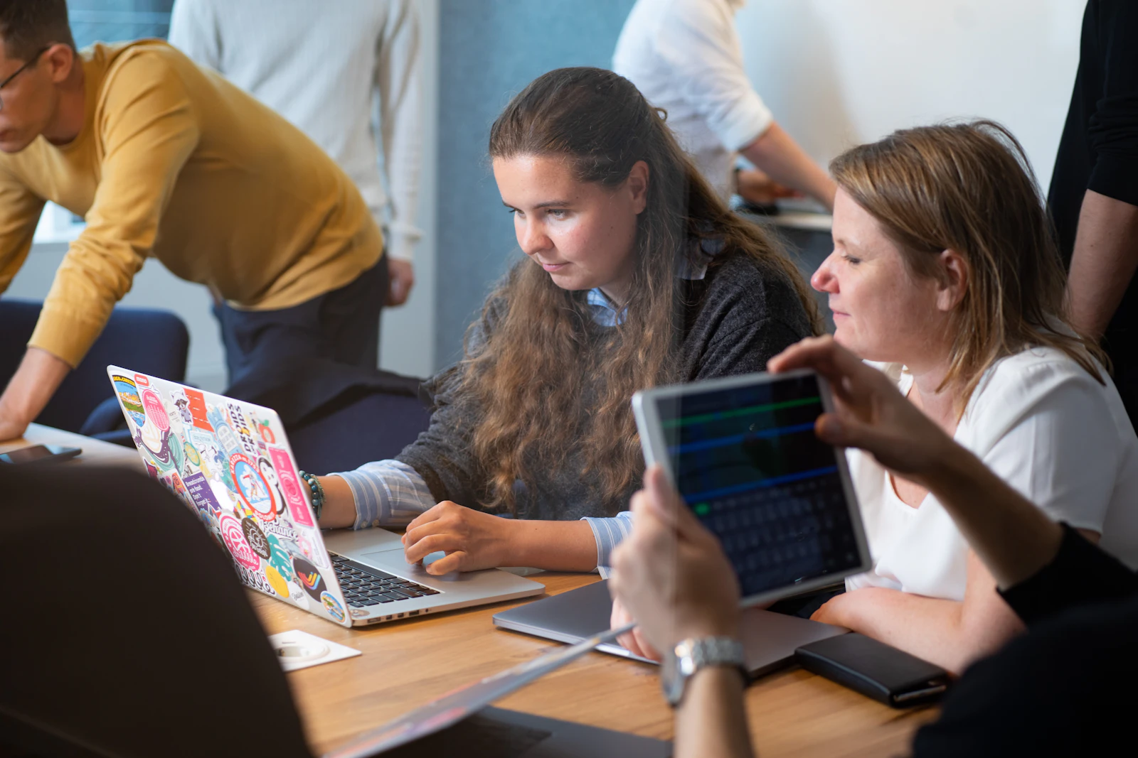 Young people working side by side at a table with laptops and a tablet