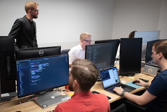 a group of men sitting at a table working on computers