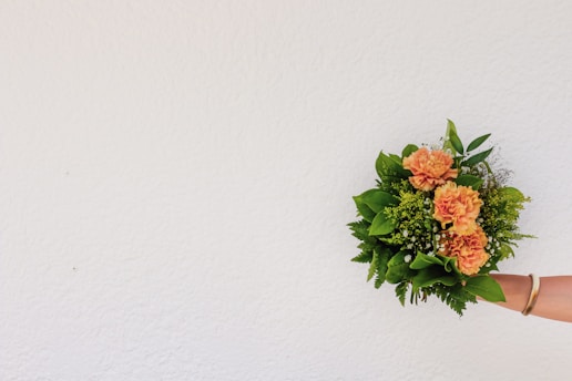 a person holding a bouquet of flowers against a white wall