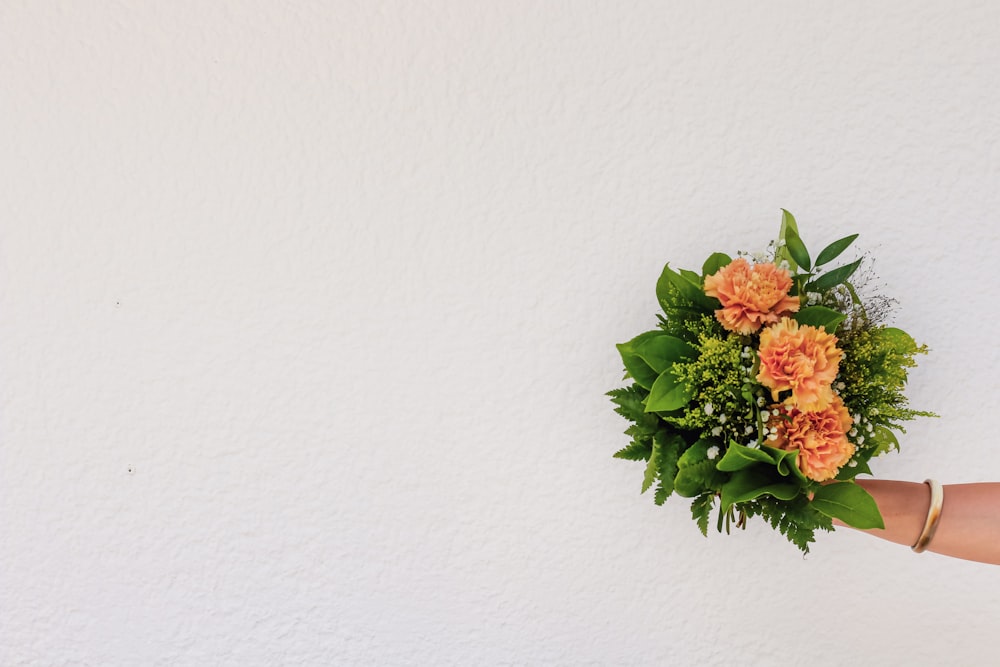 a person holding a bouquet of flowers against a white wall