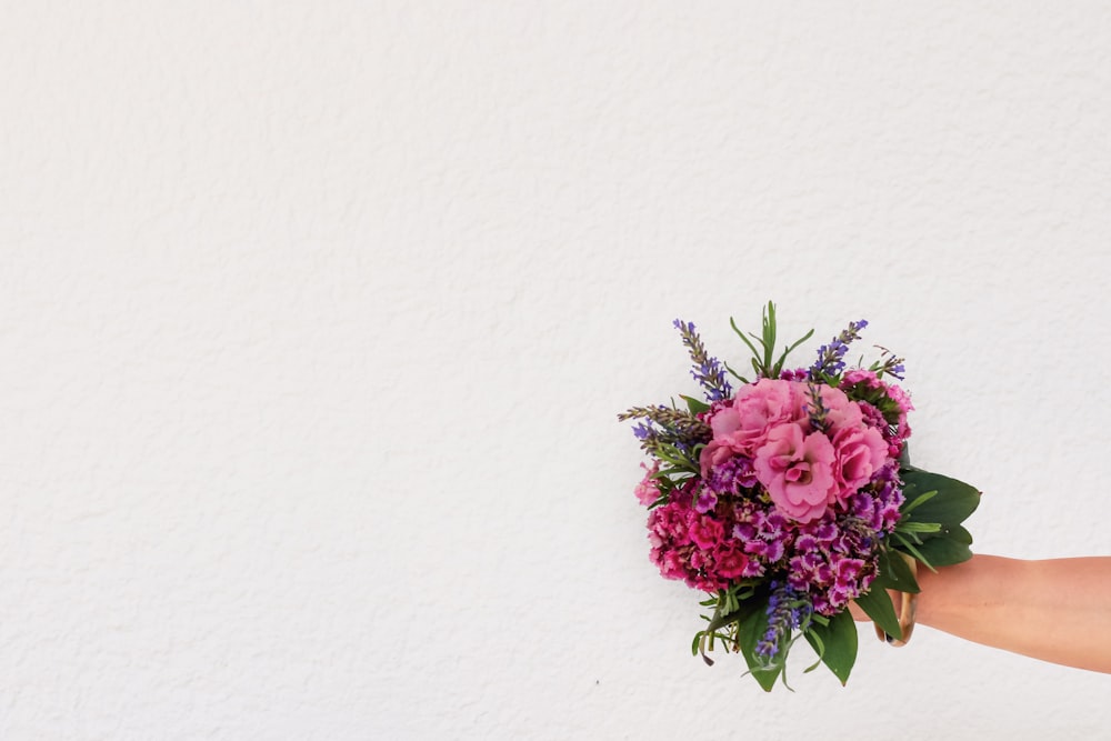 a person holding a bouquet of flowers against a white wall