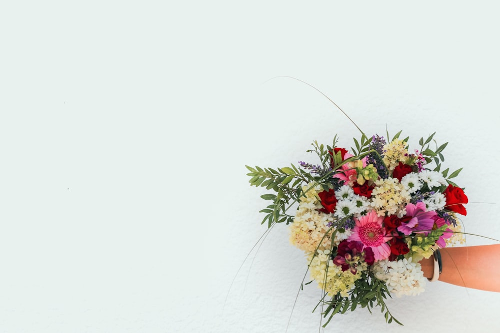 a person holding a bouquet of flowers against a white wall