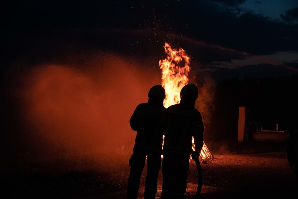 two people standing in front of a fire
