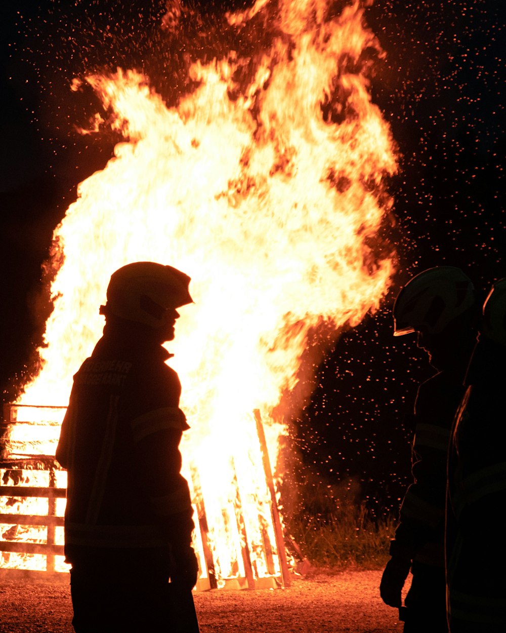 dois bombeiros em pé em frente a um grande incêndio