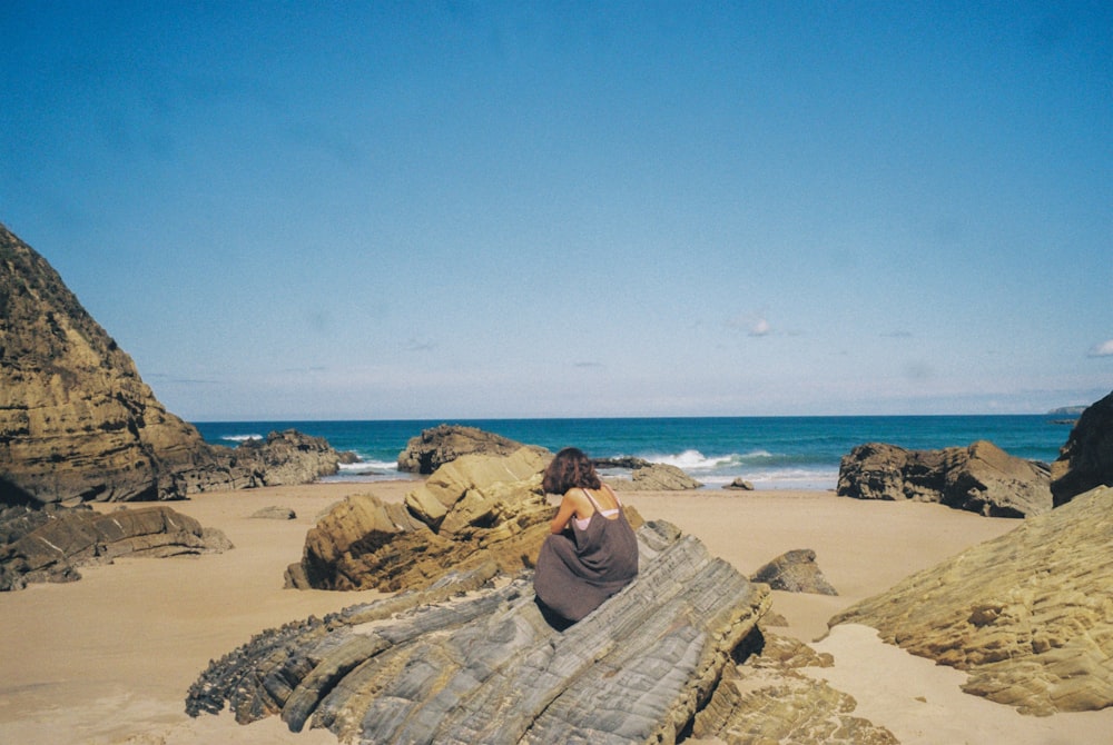 a woman sitting on a rock on the beach