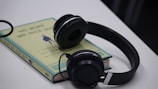 A pair of black headphones rests on top of a paperback book with the title 'No More Mr. Nice Guy' by Glover. The book is positioned on a white surface, and its cover showcases a minimalist design with text and an illustration in the center.