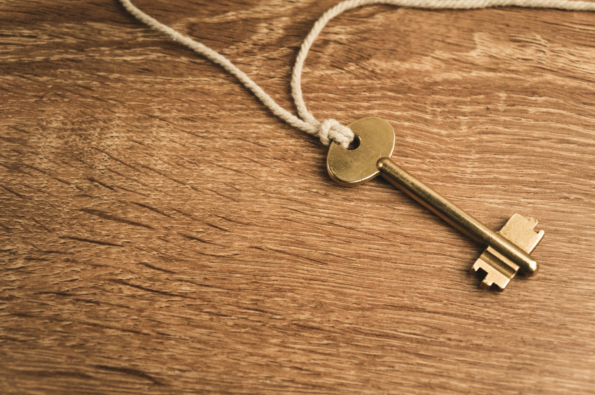 Golden key on rope on wooden background