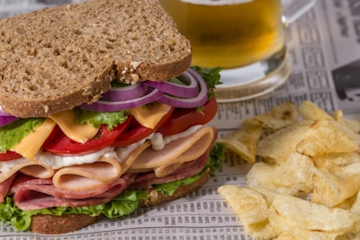 a sandwich and chips on a newspaper with a glass of beer